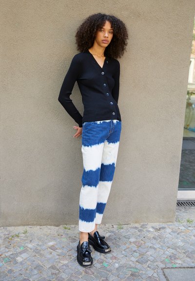 Black ribbed knit cardigan with a V-neck and button closure, paired with blue and white tie-dye straight-leg jeans and black shoes.