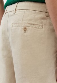 Pantaloni corti in lino beige con tasca posteriore, dotati di chiusura a bottone e logo ricamato. Tessuto liscio e design sartoriale.