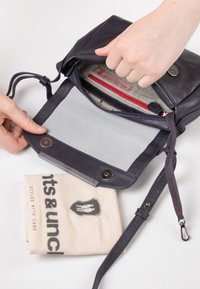 Maritieme leren handtas met een ritsluiting, grijze binnenvoering en rode accenten. Voorzien van een afneembare schouderriem en een drukknoop.