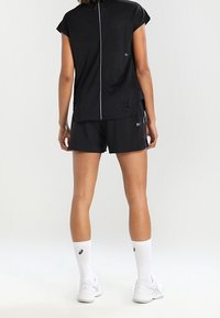 Haut de sport noir à manches courtes avec une fermeture éclair au dos, associé à un short noir. Comprend des détails de logo blancs et des chaussettes de cheville blanches avec un logo.