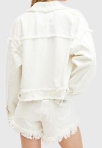 Giacca in denim bianco con bordi sfrangiati, design con colletto e due bottoni. Abbinata a pantaloncini sfrangiati coordinati, per un look armonioso.