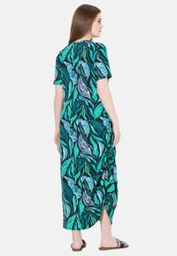 Robe maxi en tissu noir avec un motif de feuilles vertes et bleues. Manches courtes, coupe décontractée et détail de fronces sur le côté.