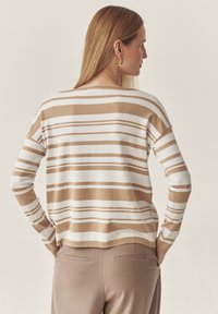 Beež ja valge triibuline sviiter, kudumise tekstuuriga, vaba lõikega ja langenud õlgadega, koos kohandatud beežide pükstega.