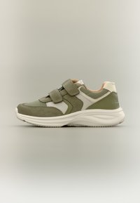 Πράσινο και μπεζ αθλητικό παπούτσι με λευκή σόλα, δύο ρυθμιζόμενους ιμάντες βέλκρο, και υφή από σουέτ και ύφασμα, εμφανίζεται από το πλάι σε ουδέτερο φόντο.