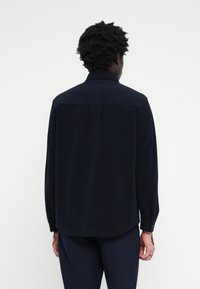 Camisa de manga larga azul marino en tela suave, con yugo trasero, puños de un botón y un corte relajado. Diseño minimalista sin adornos.