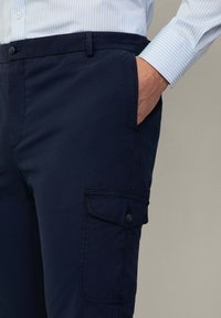 Marine cargobroek gemaakt van stevig materiaal, met zijzakken, een knoopsluiting en een gladde textuur.