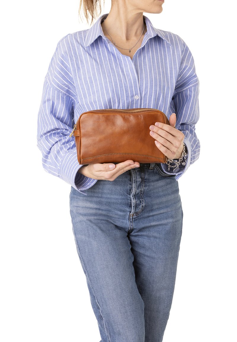 Borsa in pelle marrone con design curvo, dotata di una cerniera dorata. La superficie è liscia e viene tenuta da una persona che indossa una camicia a righe.