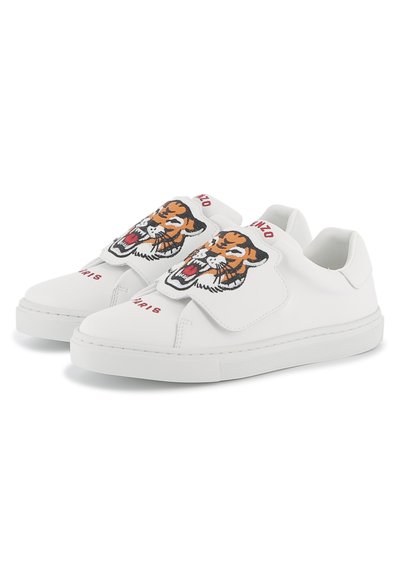 Baskets blanches avec une finition en cuir lisse, comportant un design de tigre brodé en évidence sur le rabat en velcro et une marque rouge.