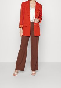 Red blazer with rolled sleeves, brown wide-leg pants, and white strappy sandals, topped with a light satin camisole. Minimalistic design.