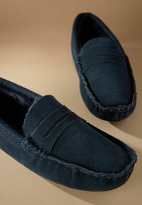 Papuci din suede albastru închis, cu interior căptușit, cusături proeminente și un model texturat subtil pe laturi.