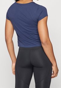 Camiseta corta azul marino de tela suave con mangas cortas, combinada con leggings negros de cintura alta que presentan detalles de costura curva.