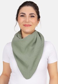 Écharpe verte en tissu doux et texturé, présentant une forme triangulaire avec un motif froissé et des bords bruts, portée autour du cou.