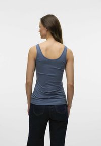 Débardeur slim fit bleu en tissu doux, avec un col rond et de larges bretelles. Associé à un jean sombre, montrant une texture lisse.