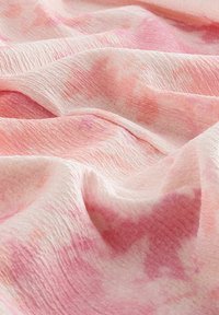 Tela de un rosa claro con una superficie suave y texturada, que presenta sutiles patrones de tie-dye en un rosa más oscuro y pliegues suaves y fluidos.