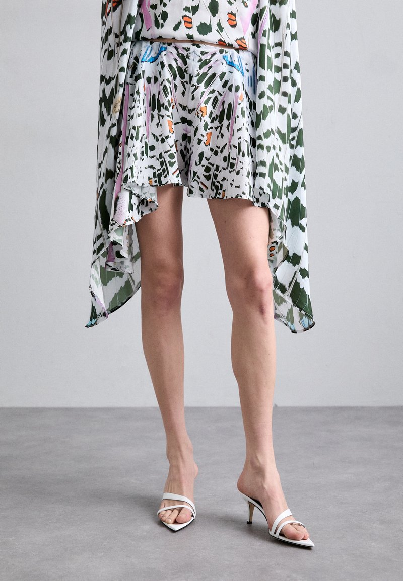 Ensemble jupe et top à motifs floraux en vert, blanc et rose, avec un design fluide et un ourlet asymétrique. Assorti à des mules blanches à talons.