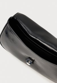 Μαύρη δερμάτινη τσάντα-φάκελος με κομψό σχεδιασμό. Διαθέτει μαγνητική κλείσιμο και λεία υφή, επιδεικνύοντας μια μινιμαλιστική αισθητική.