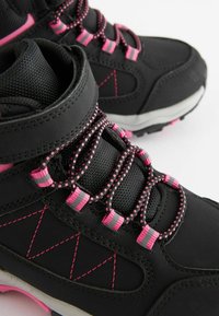 Scarponi da trekking neri con accenti rosa, dotati di pannelli in rete, lacci testurizzati e una suola in gomma resistente con dettagli rosa a contrasto.