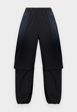 Pantalon cargo noir et bleu foncé avec taille et poignets élastiques, doté de poches latérales zippées et de panneaux en tissu superposés sur les cuisses.