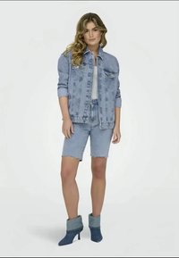 Denim jakna in kratke hlače v svetlo modri barvi z raztrganimi robovi. Ustvarjena z modrimi gležnjarji z ovitim robom. Preprost dizajn.