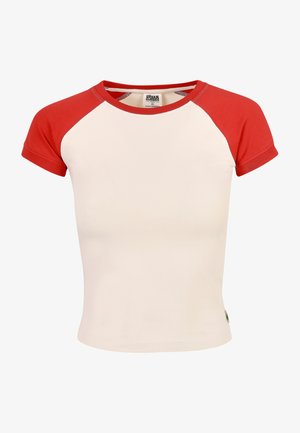 T-shirt kratkih rukava bež boje s crvenim raglan rukavima. Izrađen od glatke tkanine sa standardnim okruglim izrezom i malom oznakom na rubu.