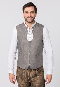 Graue Wollweste mit hohem Kragen, vorderer Knopfleiste und zwei Taschen, getragen über einem weißen Langarmhemd. Bestickte braune Hose.