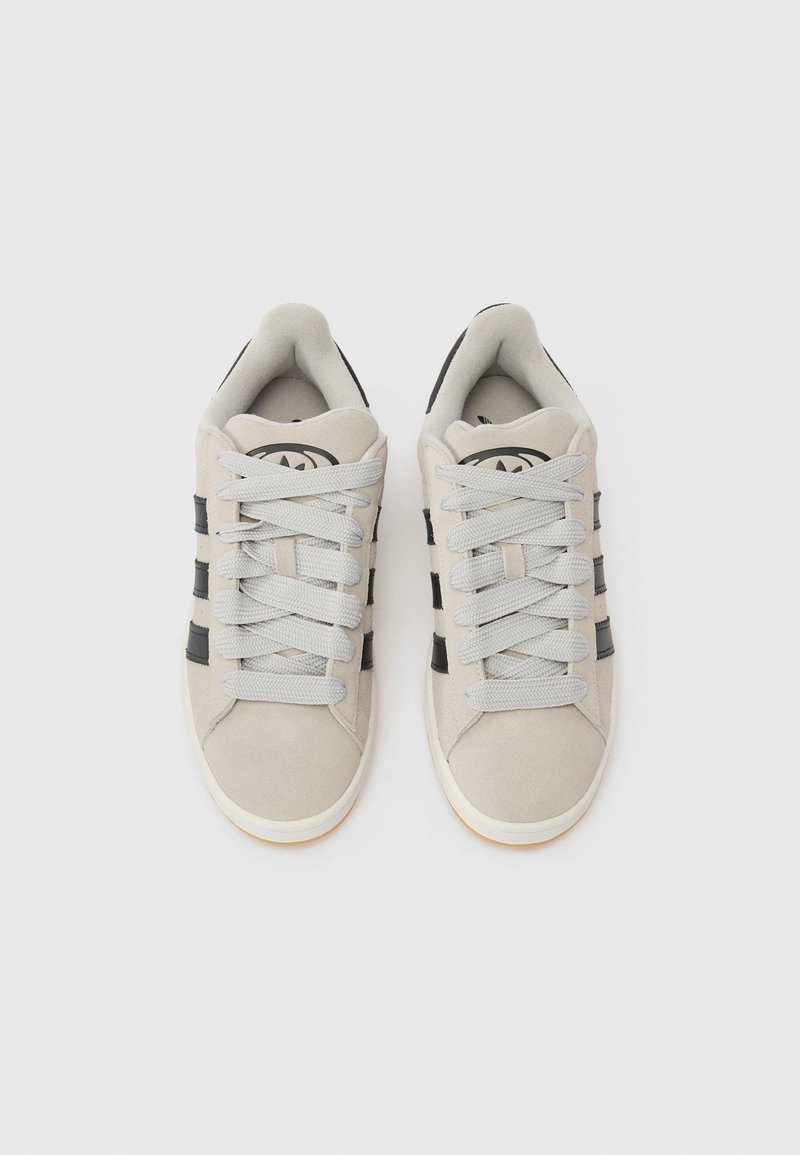 Ljusgrå sneakers med svarta ränder, med ovandel i mocka, rund tå och platta skosnören; gummisula med ljusbruna detaljer.