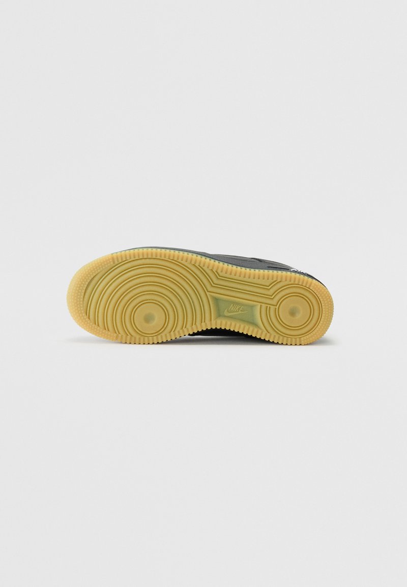 Schwarze Sneaker-Sohle mit einer strukturierten, gelben Gummi-Außensohle. Verfügt über kreisförmige Muster und das eingeprägte Nike-Logo an der Seite.