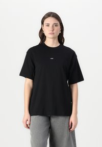 Black short-sleeve t-shirt made of cotton. Features a crew neck and a small logo in white on the chest. Paired with gray wide-leg pants.
