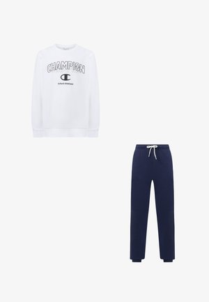 Witte Champion-trui met zwarte logo-tekst, gecombineerd met marineblauwe joggingbroek met taillekoord, tegen een witte achtergrond.