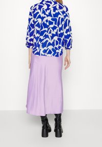 Blusa blu e bianca con motivo e maniche a tre quarti, abbinata a una gonna midi satinata lilla e stivali neri al ginocchio con tacco.