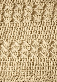 Gevlochten textiel van natuurlijke vezels in een romige beige tint, met een gestructureerd patroon van onderling geweven strengen en een open lattice-ontwerp.