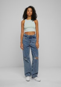 Svetlozelený bezrukávový crop top skombinovaný s voľnými svetlomodrými džínsami s roztrhnutím na stehnách, nosený s bielymi teniskami.