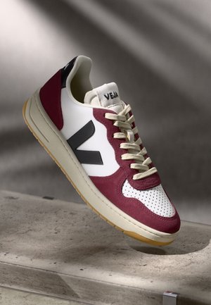 Sneaker with a white leather upper, burgundy suede accents, gray logo, beige sole, and perforated toe box. Features cream laces.