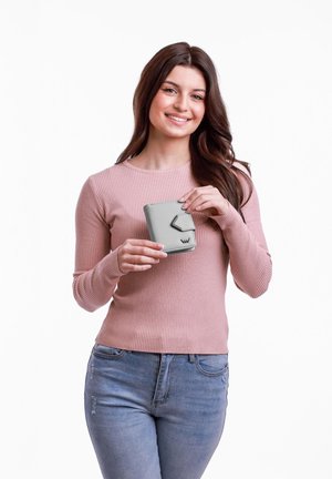 Gray wallet with a geometric flap, made of smooth material, held by a person in a light pink ribbed sweater and light blue jeans.