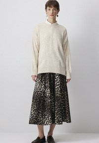 Maglione a maglia crema con colletto alto, abbinato a una gonna a stampa leopardata. La gonna presenta un design fluido e accenti scuri. Scarpe nere.