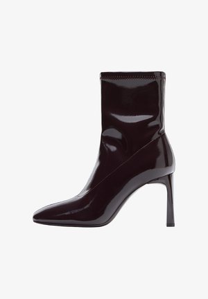 Kotníková bota s špičatou špičkou v hluboké bordó barvě z lakované kůže, s přiléhavým holeněm, elegantními liniemi a vysokým jehlovým podpatkem.