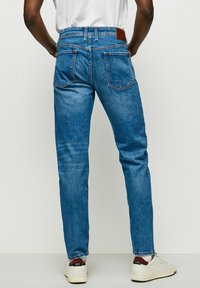 Jeans din denim albastru cu o croială dreaptă, design cu cinci buzunare, cusături vizibile și o etichetă din piele maro pe talie.