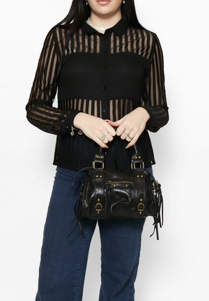 Zwarte doorschijnende blouse met verticale strepen, gecombineerd met een kleine zwarte leren handtas met gouden hardware en franjes.