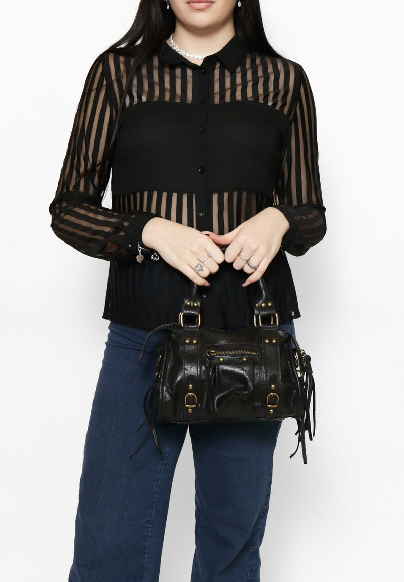 Blusa nera trasparente con righe verticali, abbinata a una piccola borsa in pelle nera con hardware dorato e dettagli in frange.