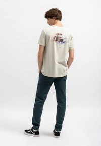 Lichtgrijze t-shirt met korte mouwen, met een kleurrafische afbeelding op de rug. Gekozen in combinatie met donkerblauwe broek en zwarte sneakers.
