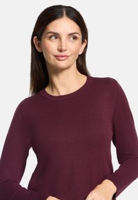 Bordeauxrode trui in een aansluitend ontwerp, gemaakt van zachte gebreide stof, met een klassieke ronde hals en lange mouwen.