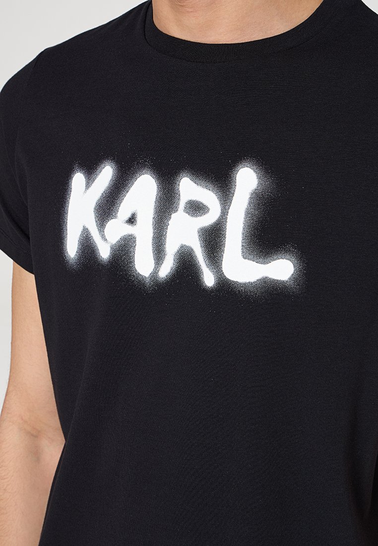 T-shirt en coton noir avec un texte en spray blanc, en lettres audacieuses, spellant "KARL" sur la poitrine. Manches courtes, col rond.