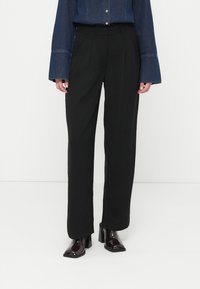 Μαύρο παντελόνι ψηλόμεσο με φαρδιά πόδια και απαλό ύφασμα. Συνδυάζεται με ένα πουκάμισο τζιν που έχει φουσκωτά μανίκια και λεπτομέρειες με κουμπιά.