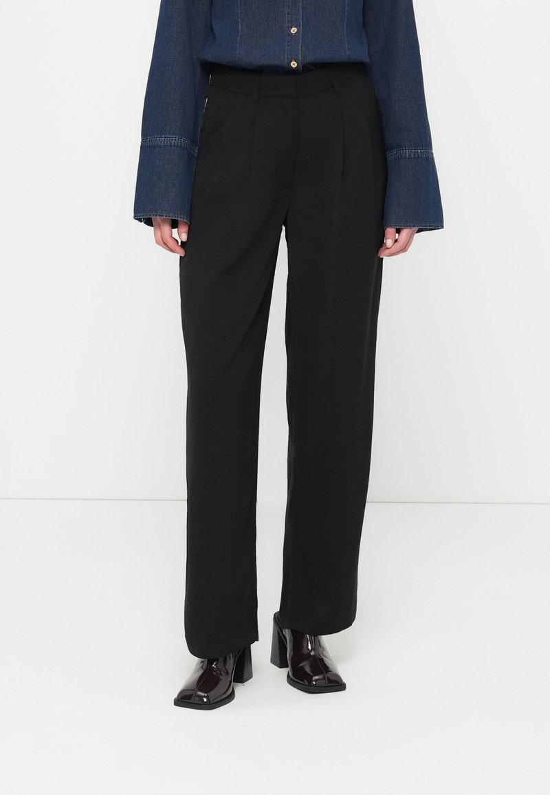 Μαύρο παντελόνι ψηλόμεσο με φαρδιά πόδια και απαλό ύφασμα. Συνδυάζεται με ένα πουκάμισο τζιν που έχει φουσκωτά μανίκια και λεπτομέρειες με κουμπιά.