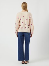 Pull en tricot rose avec des fleurs brodées dans des nuances de magenta, associé à un jean en denim bleu à jambes larges. Le pull a une coupe décontractée.