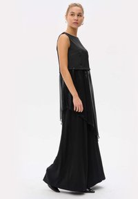 Zwarte jurk met een mouwloze top en een gelaagde, doorschijnende rok. Het ontwerp heeft een asymmetrische zoom en een gladde, vloeiende textuur.