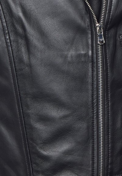 Zwarte leren jas met een gladde textuur, zilveren rits en gedetailleerde stiksels langs de randen. Close-up van de rits en het materiaal.