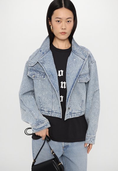 Svijetloplava skraćena traper jakna s čvrstim ovratnikom, kopčanjem na gumbe i izbjeljenim detaljima, preko crne majice s grafikom.