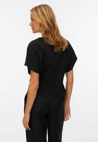 Czarny krótki top z dopasowanym krojem, gładką fakturą, lekko rozszerzanymi rękawami oraz subtelnym detalem w postaci szwu z tyłu.