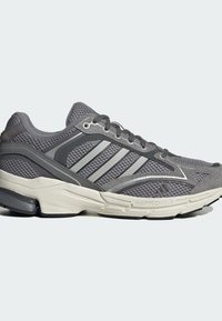 Baskets de sport grises avec panneaux en mesh et en suède, trois bandes argentées sur le côté, semelle blanche coussinée et semelle extérieure noire.